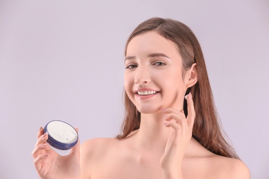 Photo of Teenage girl with acne problem using cream against grey background