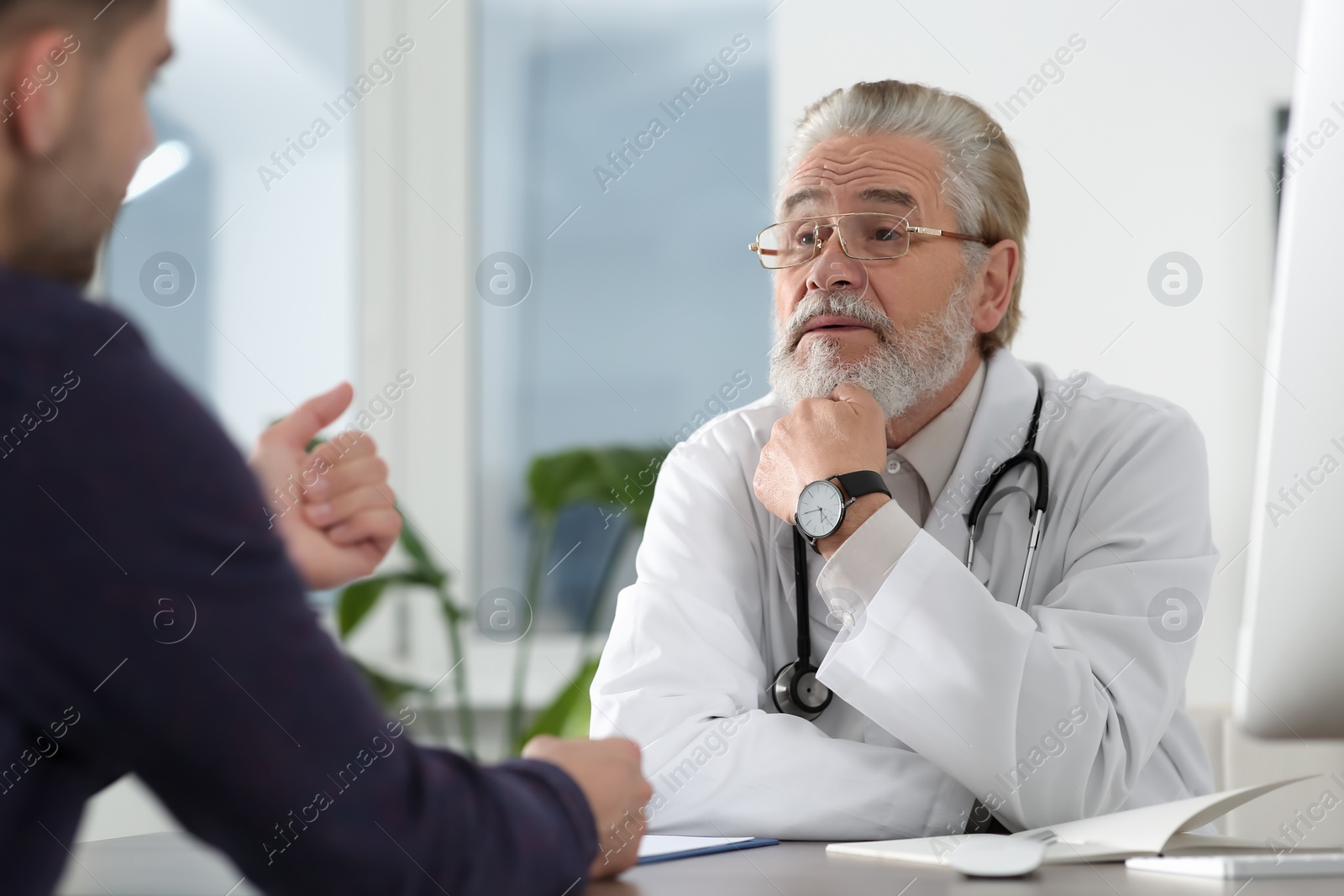 Photo of Senior doctor consulting patient at wooden table in clinic