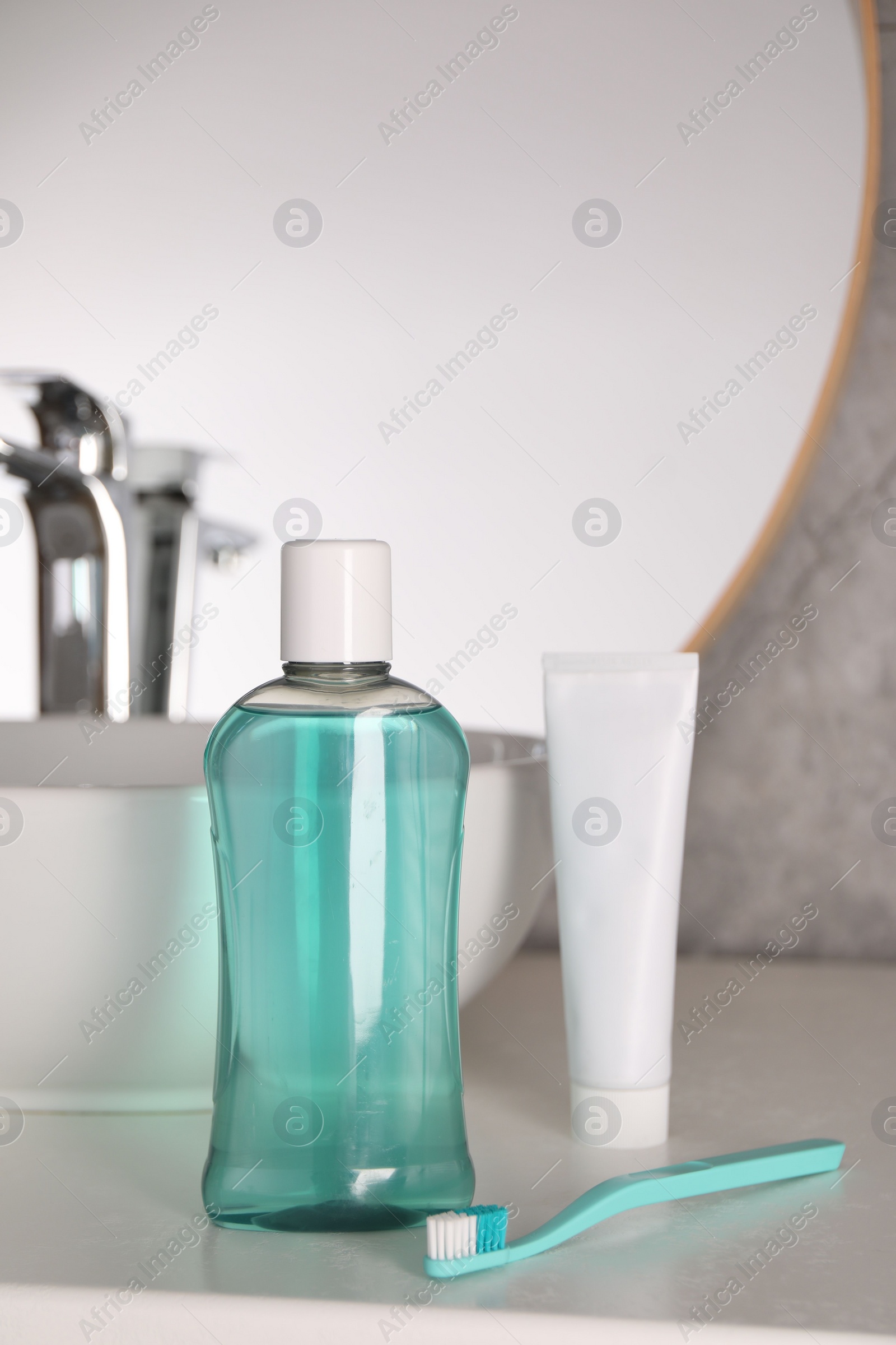 Photo of Bottle of mouthwash, toothpaste and toothbrush on light countertop in bathroom