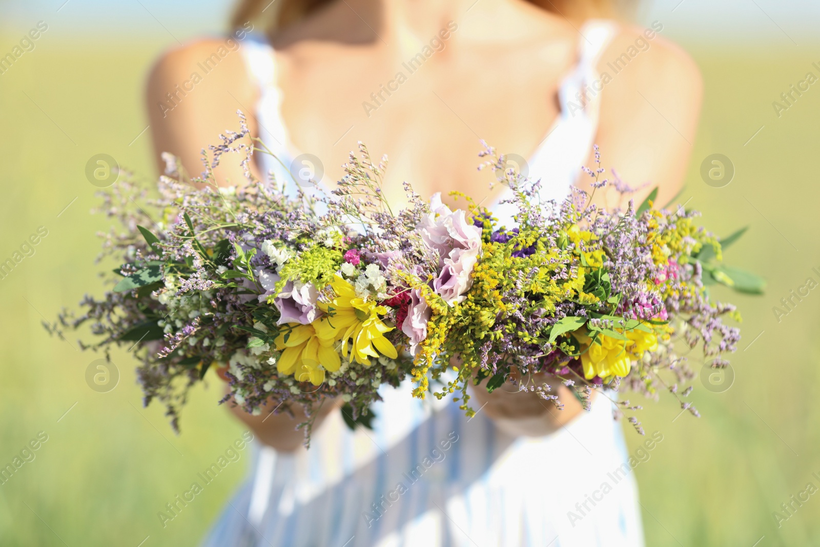 Photo of Young woman holding wreath made of beautiful flowers in field on sunny day, closeup