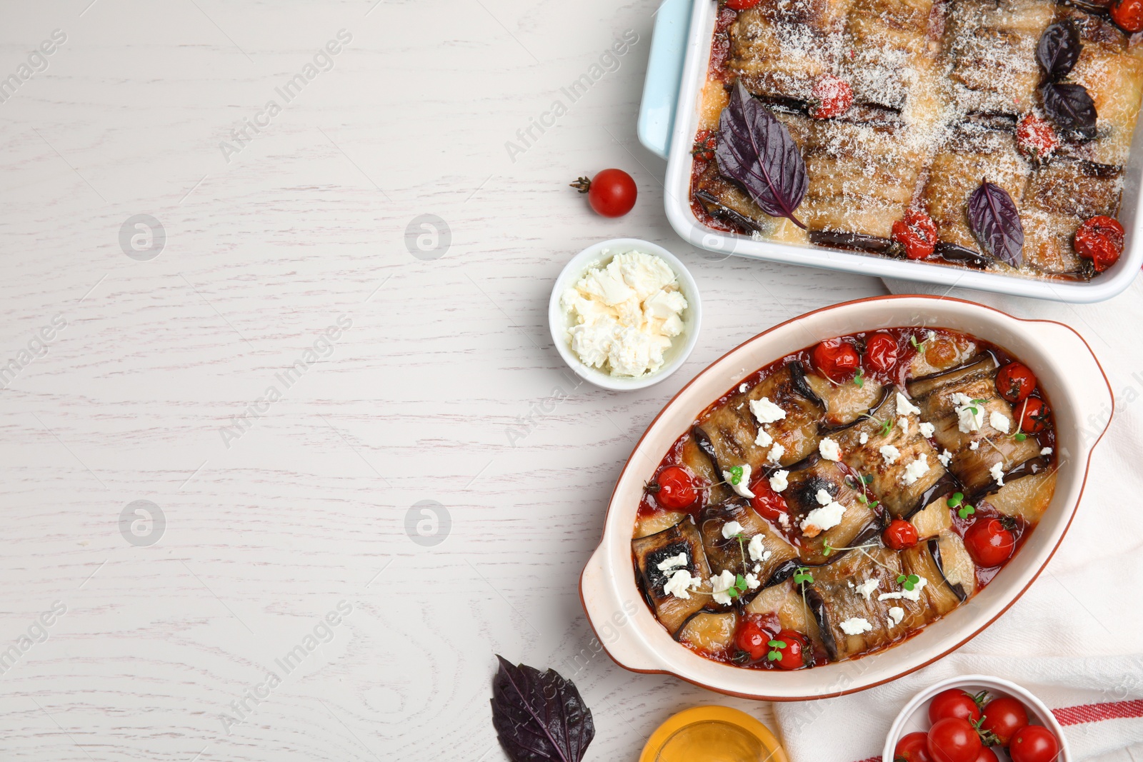 Photo of Tasty eggplant rolls in baking dishes on white wooden table, flat lay. Space for text