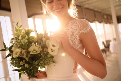 Photo of Bride in beautiful wedding dress with bouquet in restaurant, closeup