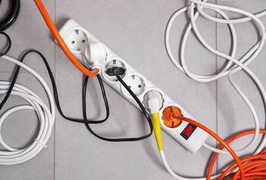 Photo of Power strip with electrical plugs on grey floor, flat lay