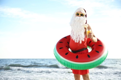 Photo of Santa Claus with cocktail and inflatable ring on beach, space for text. Christmas vacation