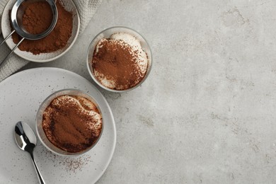 Delicious tiramisu in glasses, cookies and sieve with cocoa powder on light table, flat lay. Space for text