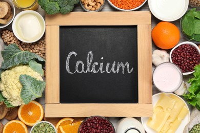Photo of Set of natural food and chalkboard with written word Calcium on white wooden table, flat lay