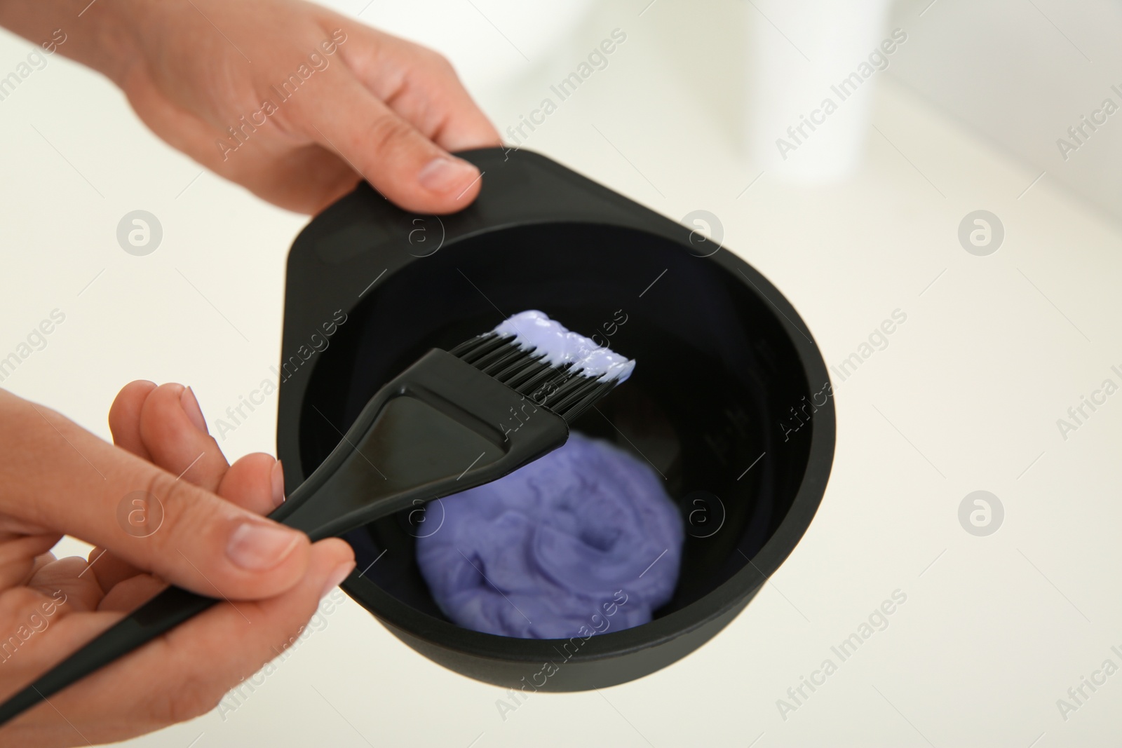 Photo of Woman preparing hair dye in bowl at white table, closeup