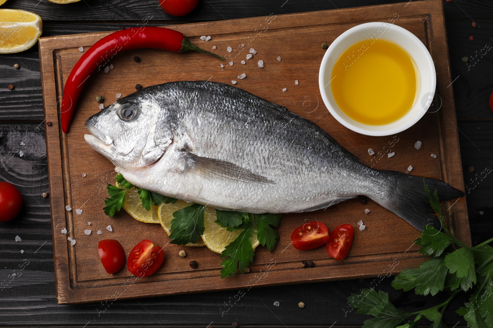 Photo of Flat lay composition with fresh raw dorado fish and spices on black wooden table