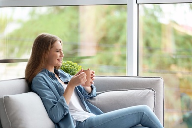 Photo of Young beautiful woman drinking morning coffee near window at home