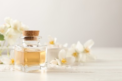 Beautiful composition with jasmine essential oil and fresh flowers on white wooden table. Space for text