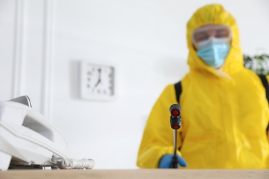 Photo of Employee in protective suit sanitizing office. Medical disinfection, focus on spray