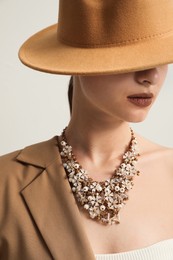 Young woman wearing stylish clothes and luxury necklace on light background