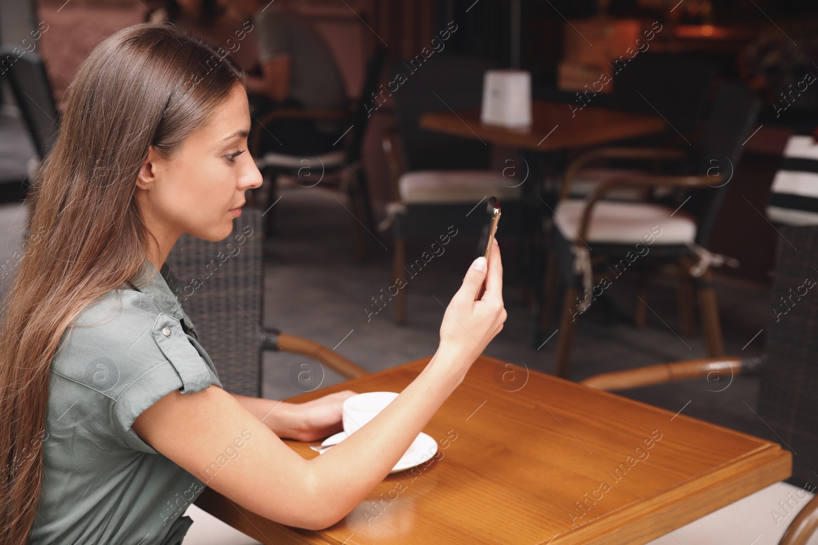 Photo of Young woman unlocking smartphone with facial scanner in outdoor cafe. Biometric verification