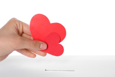 Photo of Woman putting red hearts into slot of donation box against white background, closeup