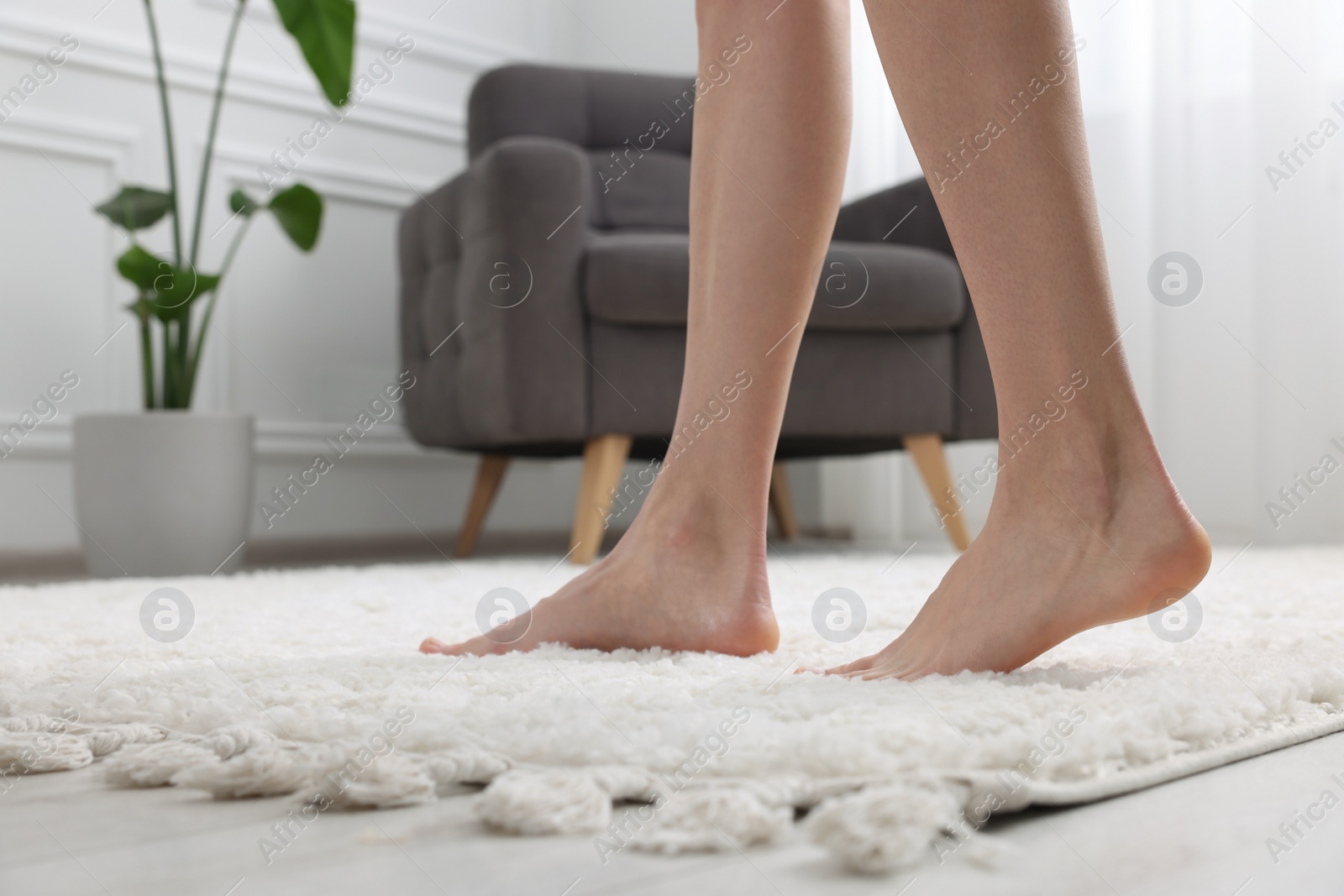 Photo of Woman walking on soft white carpet at home, closeup. Space for text