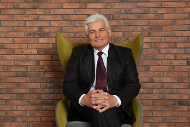 Photo of Happy mature businessman sitting in armchair near brick wall