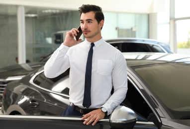 Young man talking on phone near car in modern dealership