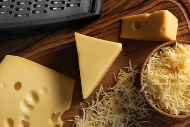 Grated, cut cheese and grater on wooden table, flat lay