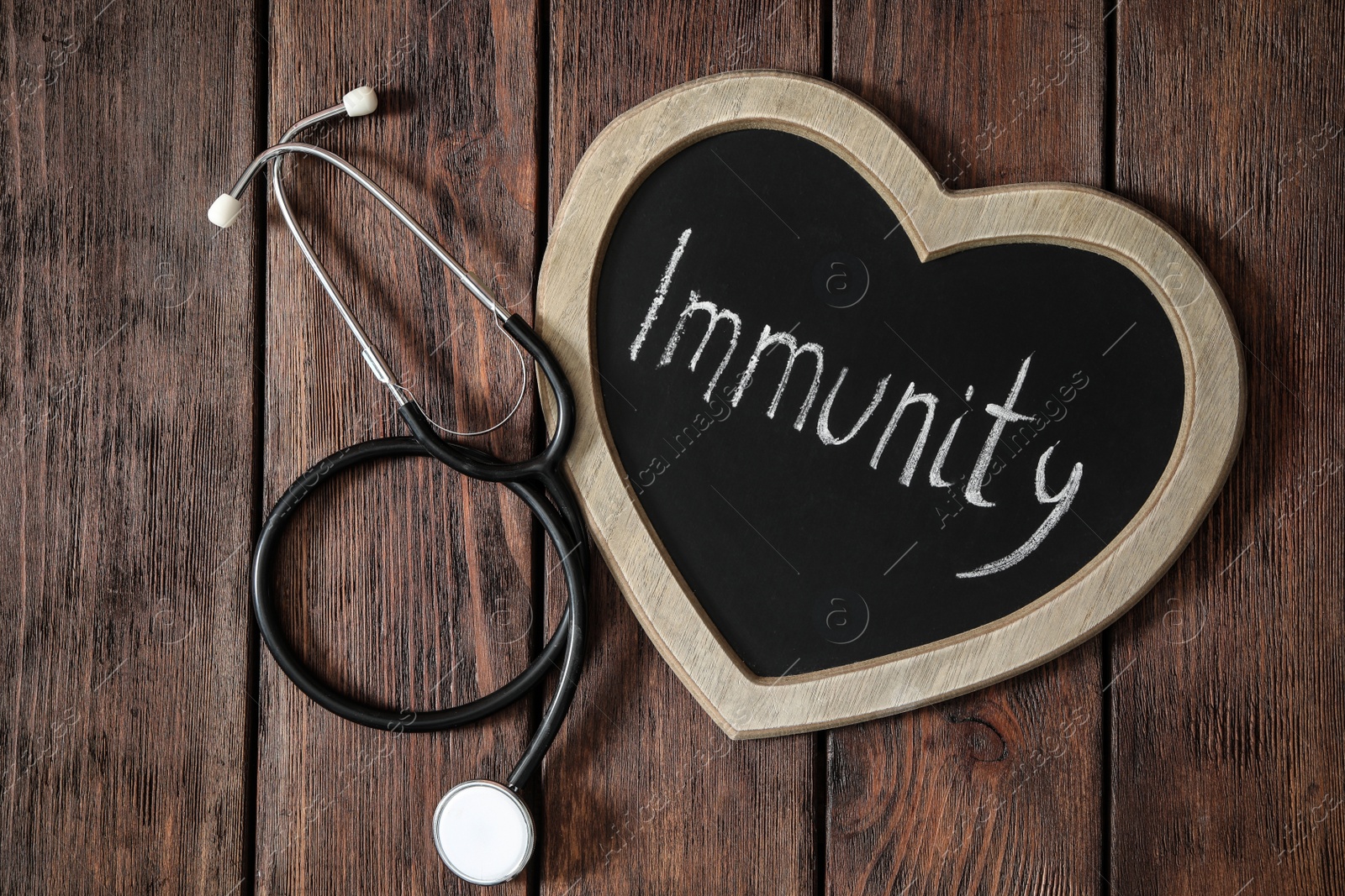 Photo of Heart shaped chalkboard with word Immunity and stethoscope on wooden table, flat lay