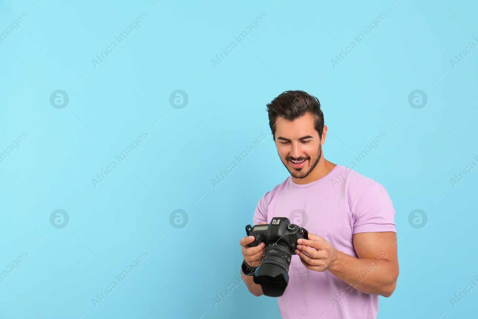 Photo of Young photographer with professional camera on light blue background. Space for text