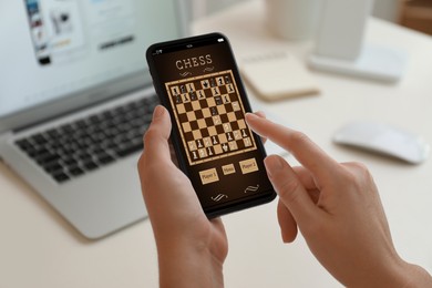Image of Woman playing online chess on smartphone at table, closeup