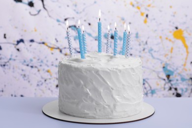 Delicious cake with cream and burning candles on light blue table