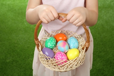 Photo of Little girl with basket full of Easter eggs on green grass, closeup