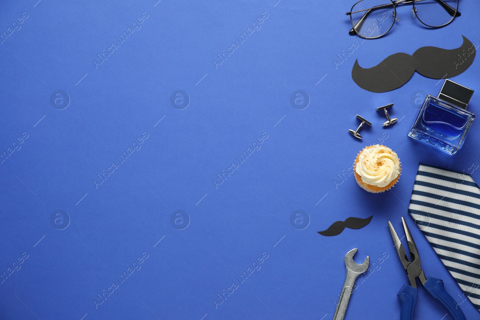 Photo of Father's day celebration. Delicious cupcake, paper mustache and men accessories on blue background, flat lay. Space for text