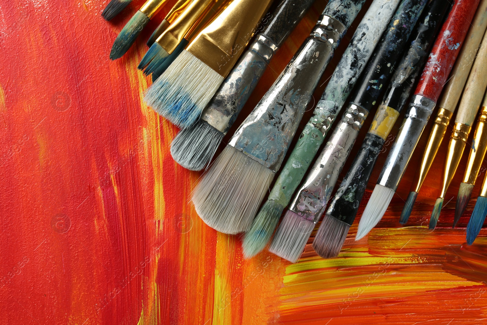 Photo of Set of different brushes on abstract colorful paint, top view