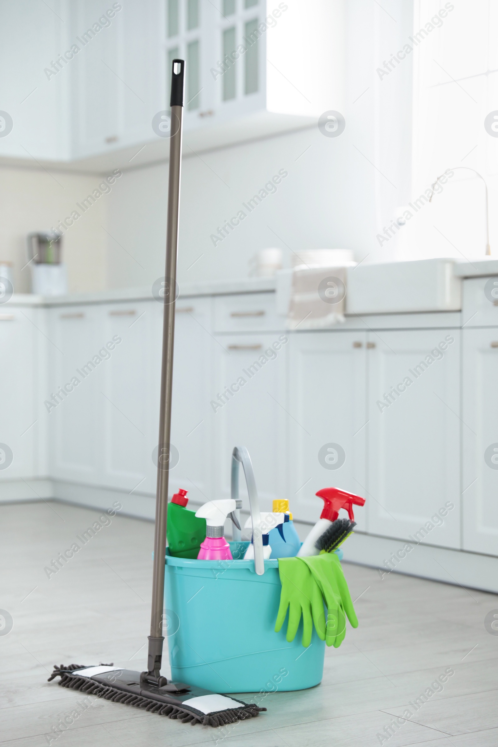 Photo of Mop and plastic bucket with different cleaning supplies in kitchen