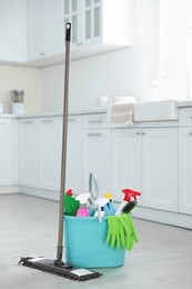 Mop and plastic bucket with different cleaning supplies in kitchen