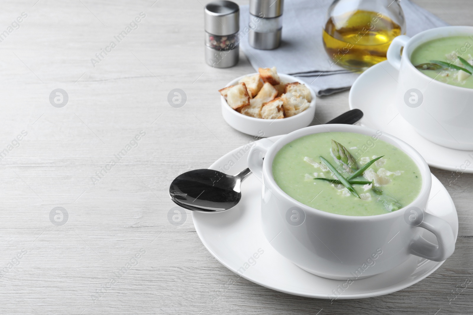 Photo of Delicious asparagus soup with green onion served on white wooden table, space for text