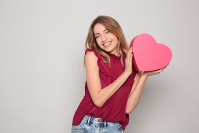 Portrait of beautiful smiling girl with heart shaped gift box on light background. International Women's Day