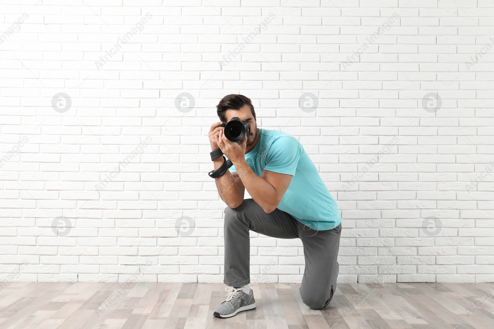Photo of Young professional photographer taking picture near brick wall