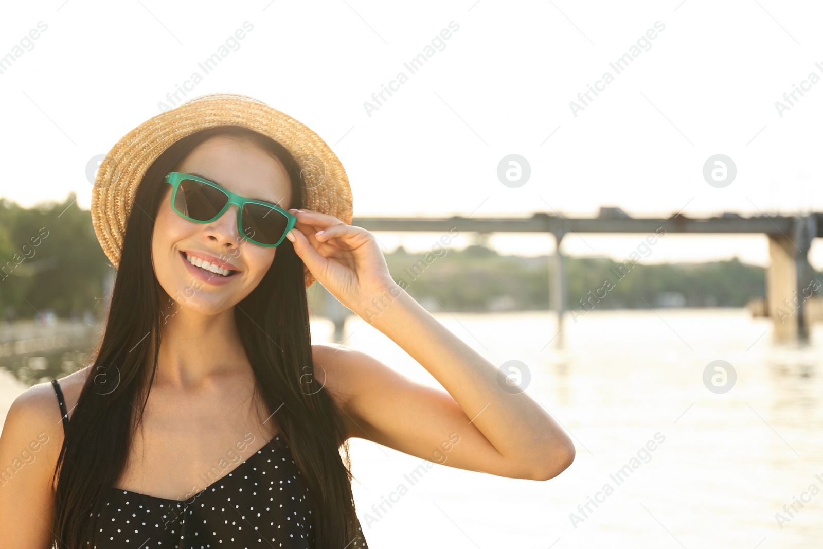 Photo of Beautiful young woman wearing stylish sunglasses near river. Space for text