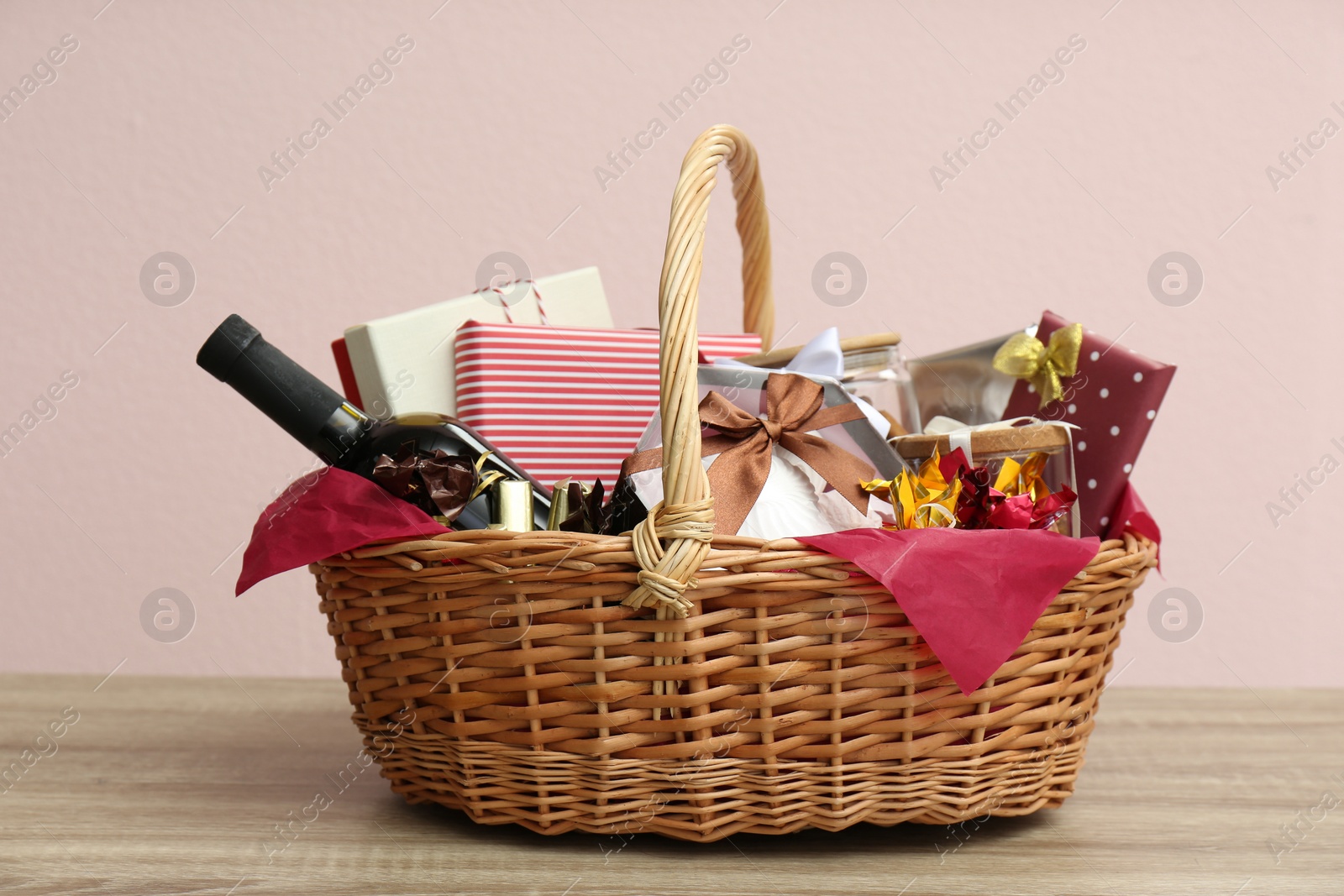 Photo of Wicker gift basket with bottle of wine on wooden table