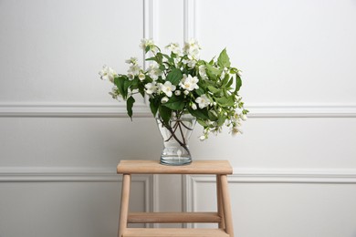 Photo of Beautiful bouquet with fresh jasmine flowers in vase on wooden table indoors