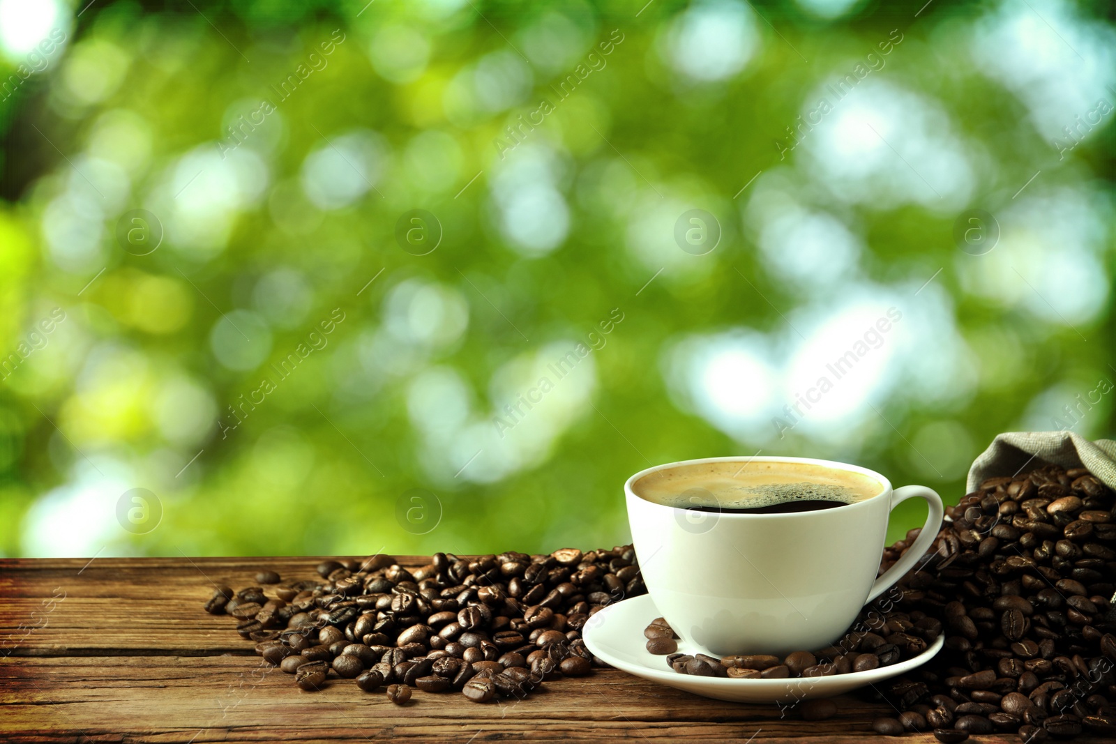 Image of Cup of aromatic hot coffee and beans on wooden table outdoors. Space for text