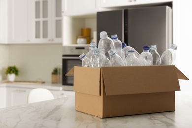 Cardboard box with used plastic bottles on table in kitchen, space for text. Recycling problem