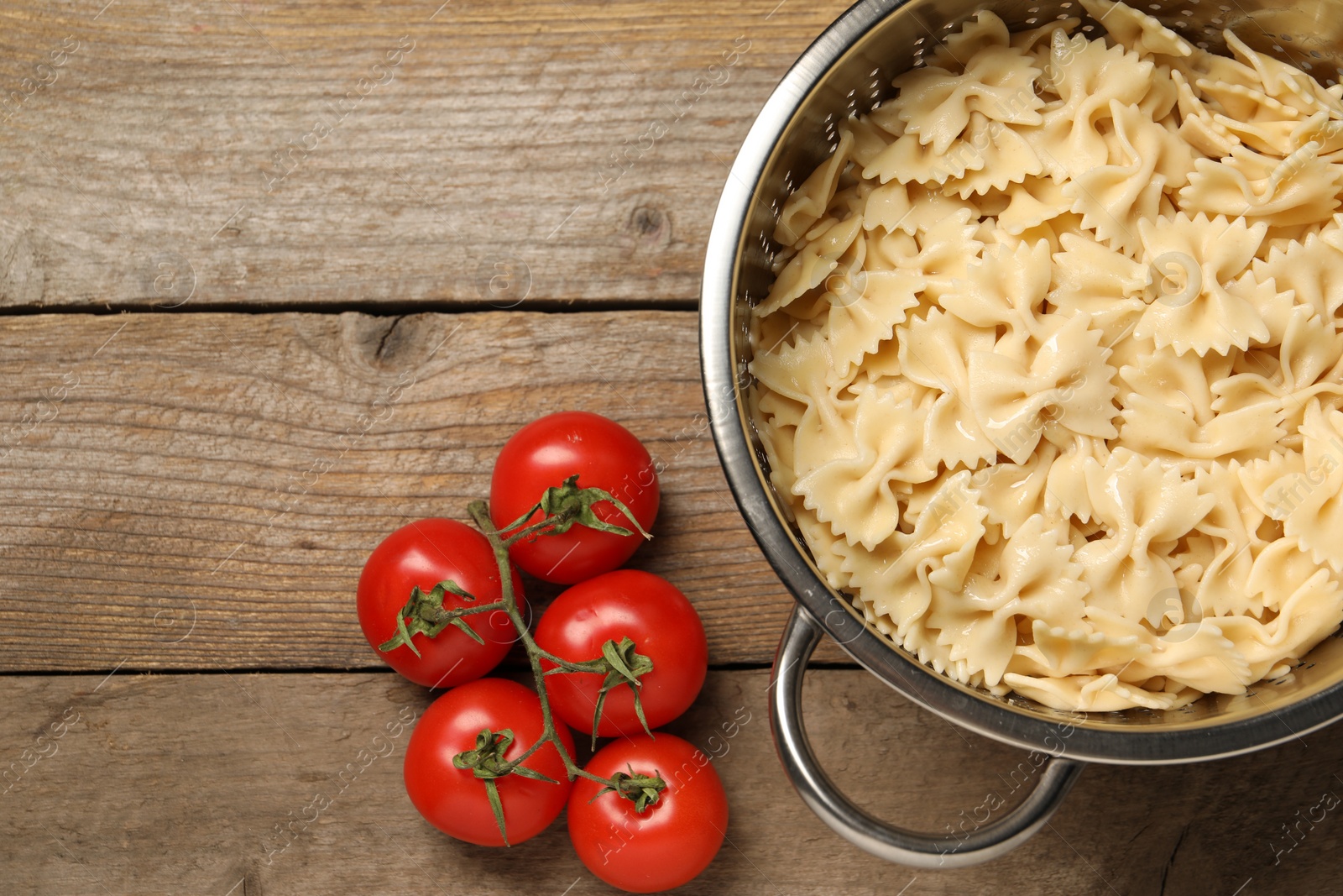 Photo of Cooked pasta in metal colander and tomatoes on wooden table, top view. Space for text