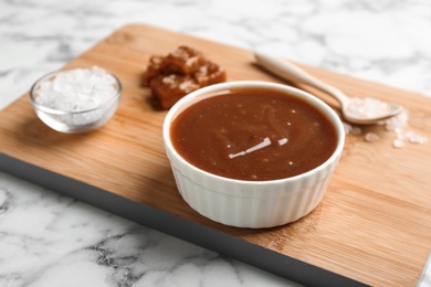 Photo of Board with bowl of caramel sauce on marble table, closeup. Space for text