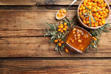 Photo of Delicious sea buckthorn jam and fresh berries on wooden table, flat lay. Space for text