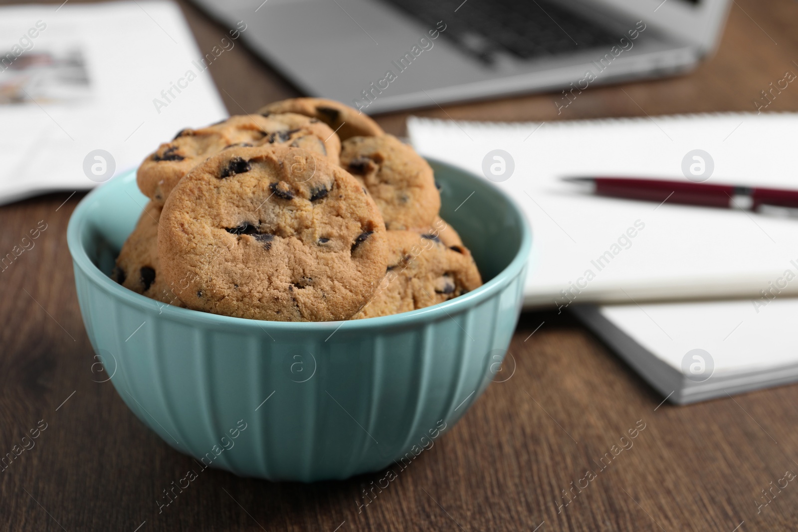 Photo of Bowl with chocolate chip cookies on wooden table in office, closeup