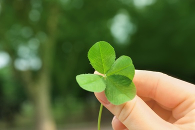 Photo of Woman holding four-leaf clover outdoors, closeup with space for text
