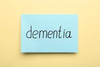 Photo of Paper note with word Dementia on beige background, top view