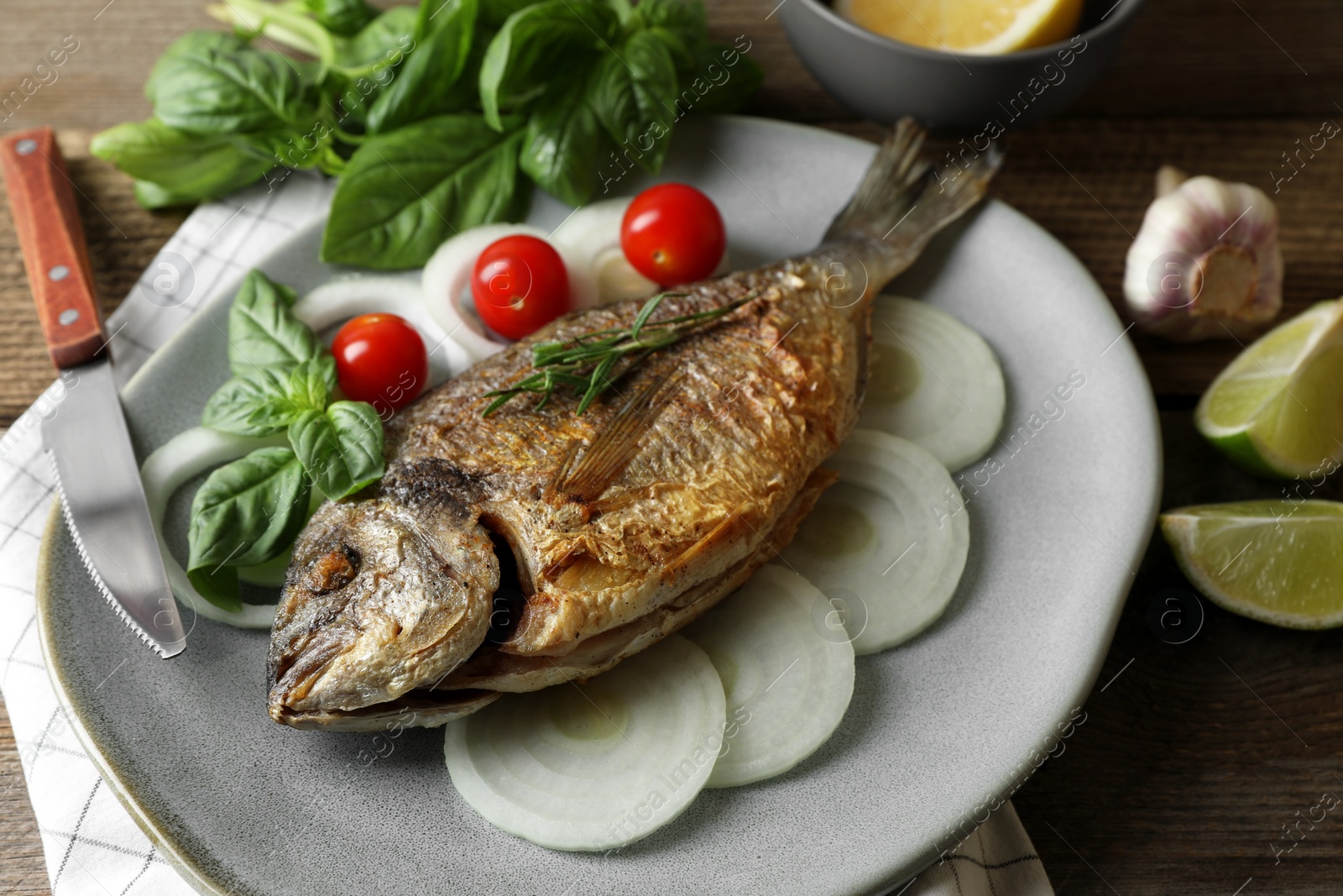 Photo of Delicious dorado fish with vegetables and herbs served on wooden table, closeup