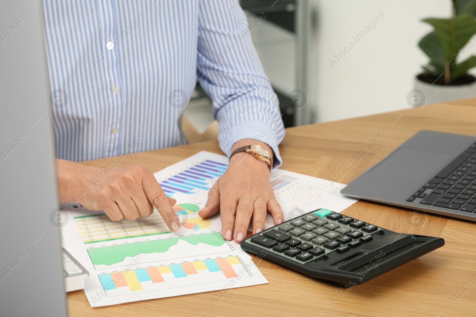 Photo of Accountant using calculator at wooden desk in office, closeup