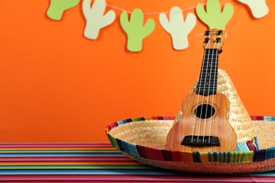 Mexican sombrero hat and ukulele on color table, closeup. Space for text