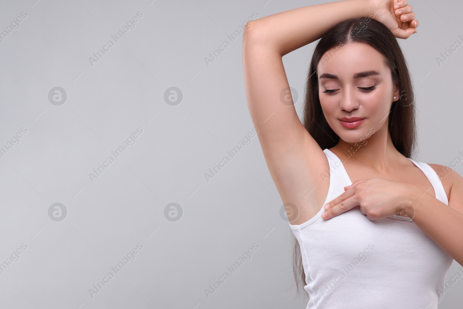 Photo of Beautiful young woman doing breast self-examination on light grey background, space for text