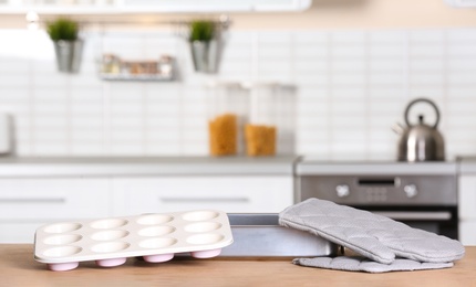 Clean baking dish, muffin pan and oven glove on table in kitchen. Space for text